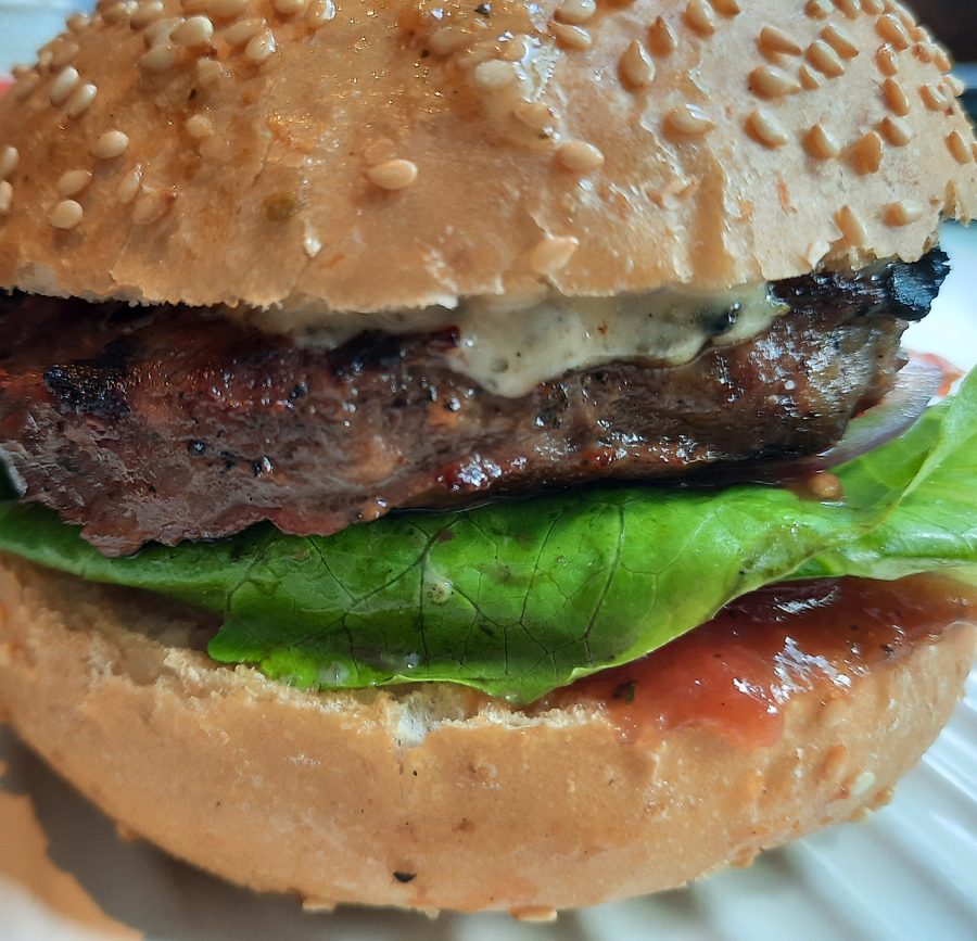 Close-up of a grilled cheeseburger with sesame bun, lettuce and sauce
